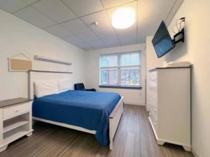 Sober living home bedroom with bed, dresser, and window, illustrating affordable recovery options.